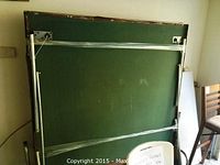 Photo of the ping pong table folded up and standing vertically, showing green playing surface and metal support structure