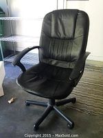 Front and angled view of a black office chair on wheels with padded armrests and segmented backrest stitching, showing some tears on the backrest.