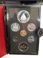 Coins displayed inside original black textured case showing seven proof coins including silver dollar with Parliament design and date 1876-1976.