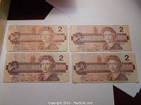 Four original Canadian two dollar bills from 1986 laid out on a white surface, showing front side with portrait of Queen Elizabeth II and denomination.