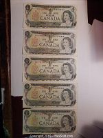 Five circulated 1973 Canadian one dollar bills on a white surface, each featuring Queen Elizabeth II and bilingual text in English and French.