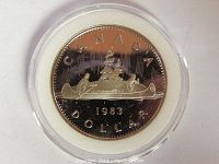 Close-up image of the 1983 Canadian silver dollar coin housed in a clear plastic case showing the detailed canoe and figures design.