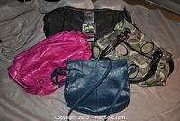 Four purses displayed together including pink, blue, black Coach, and grey patterned purse