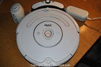 Top-down view of Roomba with accessories behind (home base, virtual wall, adapter)