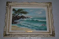 Full front view of oil painting depicting a beach with waves, rocks, a tree, set in ornately carved frame with nameplate.