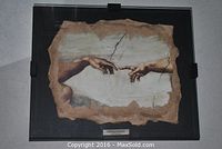 Front view of the plaque showing the hands from The Creation of Adam fresco by Michelangelo with a black frame and mounting clips.