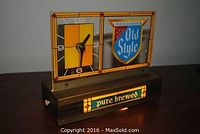 Front angle showing clock side with black and yellow face, and the blue Heileman's Old Style shield logo on the right, plus illuminated base with 'pure brewed' text.