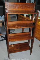 Front view of the antique bookshelf showing all four tiers and the carved scroll detail on the top panel.