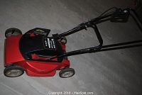 Side angled view of red and black electric lawn mower with folding handle extended and visible wheels.