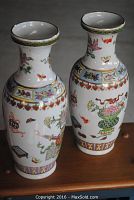 Two matching Asian porcelain vases with colorful flower and butterfly painted motifs shown together on wooden surface.