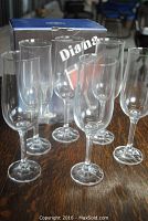 Six clear glass champagne flutes arranged in front of their original box labeled Diana.