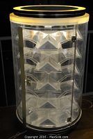 Front view of vintage Peugeot cylindrical display case showing illuminated lid, transparent body, and five clear plastic shelves inside.