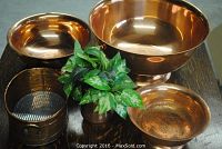 Top view of all copper pots and artificial plant container displayed on a wood surface, showing different sizes.