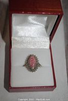 The ring displayed in red jewelry box with white interior, showing the top view of the marquise rhodochrosite stone and silver setting.