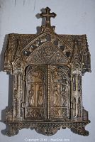 Front view of the closed triptych shrine showing detailed brass-like metal cathedral doors with relief figures and gothic design.