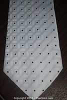 Close-up image showing the tie tip with cream/light background and repeating geometric embossed squares with small black diamond shapes inside