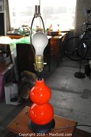 Full lamp showing the orange ceramic base with double gourd shape, metal harp, socket, and light bulb installed and unplugged.