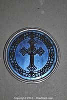 Circular crucifix plaque with ornate metal scrollwork on cobalt blue glass photographed against grey background