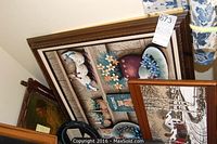 Several pieces of wall art stacked, showing wooden frames and the back of a framed print
