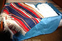 Blue faux leather folding suitcase partially open showing colorful striped blanket with fringed edges and white linens inside