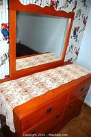 Front view of wooden dresser with lace runner and attached removable mirror with wooden frame.