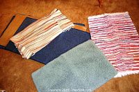Photo of six rugs arranged on carpeted floor: three blue rugs, one green rug, one pink rug, one long multicolor striped runner.