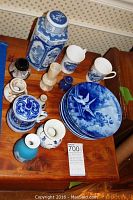 Photo of lot showing various blue and white decorative plates, Wedgwood vase, cups, and small decorative items all arranged on wooden surface