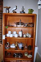 Overview of wooden shelf displaying mugs, glass bird figurines, oil lamp, decorative ceramics, small bowls, and teapots.