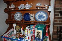 Photo of shelves showing floral porcelain tea set, blue and white plates, angel figurine, glass vase, snowman and Santa holiday decorations, and boxed musical water globe.