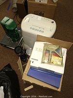 Photo of a white paper shredder, green coffee maker with no pot, and boxes including binders.