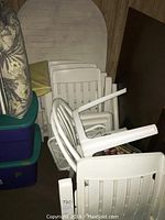 Photo showing stacked white plastic chairs and cushions next to plastic containers, illustrating the chairs and additional items in the lot.