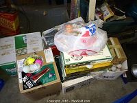 Boxes stacked containing assorted used golf balls with a plastic bag of golf tees on top.