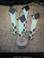 Five bird feeders arranged on a brick-paved surface, showing four tall vertical tube bird feeders with feeding holes and roofs, and one round bird feeder.