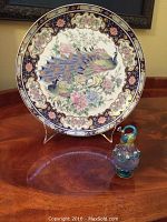 Photo showing the full view of the decorative plate with colorful peacock and peonies design and the peacock-shaped perfume bottle beside it.
