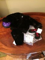 Photo showing black faux fur jacket, infant shoes, velvet hat, baby bunting with matching hat, and moon and stars night light on wooden surface.