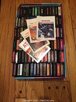 Box of over 90 Atari 2600 game cartridges with four game manuals on top including one for Asteroids.