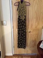 Full-length front view of the black Adrianna Papell gown with gold beaded floral and geometric patterns, hanging on a door.