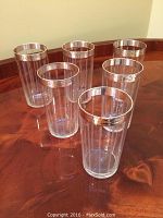 Set of six clear iced tea glasses on a wooden surface, showing the sterling silver hammered rims and etched vertical lines on the glass bodies.