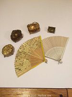 All items arranged on surface including four trinket boxes and two hand fans visible together.