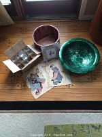 Photo showing full home decor lot with large peacock green bowl, wooden bowl, cardboard box with glass tea lights, and double-sided Japanese artwork laid out on wood floor.