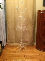 Full view of the white metal wire mannequin on stand against a beige curtain background showing overall height and design.