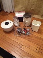 Photo showing the Juiceman II juicer with attachments, OXO salad spinner, Cuisinart mini-prep, Mini-Mate cooler, adjustable sink tray, and egg fry rings on wooden floor.