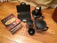 Photo of Ninja blender motor base and attachments alongside stacked cookbooks and Villaware waffle maker showing waffle plates open.