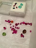 View of various loose gemstones on table including round and oval red stones, green and brown round stones