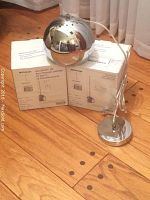 Two chrome finish BoConcept ball pendant lights, each spherical and about 18cm in diameter, shown standing on wooden floor next to two BoConcept branded boxes.