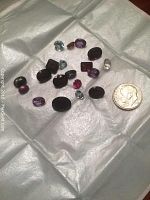 Top down view of 20 assorted loose gemstones including garnets, sapphires, amethysts, and topaz, shown next to a dime for size reference.