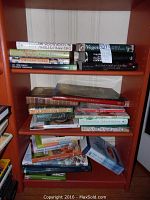 Books on wooden bookshelf showing various cookbook titles and spines, stacked horizontally and vertically.