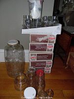Group of over 75 Kerr Mason jars with some spare lids in containers, boxes of unopened Mason jars stacked behind.