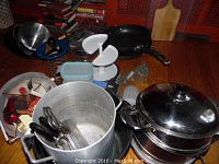 Wide view showing multiple kitchen items including stock pot, Asian steamer, utensils and containers on wooden surface.