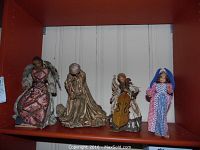 Four antique figurines displayed on a shelf: two wax angels, one straw doll, and one country-style angel figurine